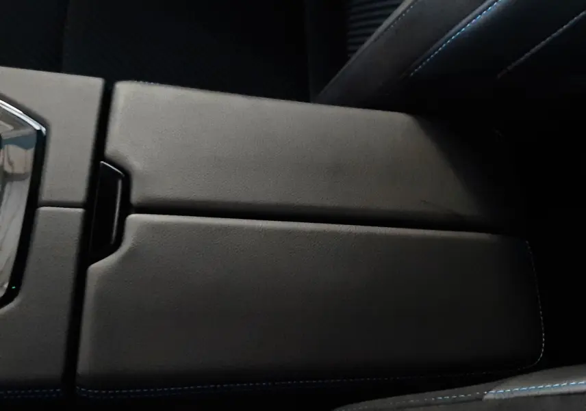 Vue rapprochée de l'accoudoir central noir avec surpiqûres bleues à l'intérieur du Renault Austral E-Tech Hybrid 2025.