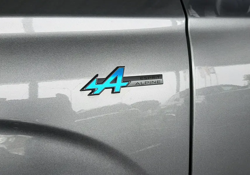 Gros plan sur l’écusson bleu "Esprit Alpine" sur la porte gris schiste satin du Renault Austral 2025.