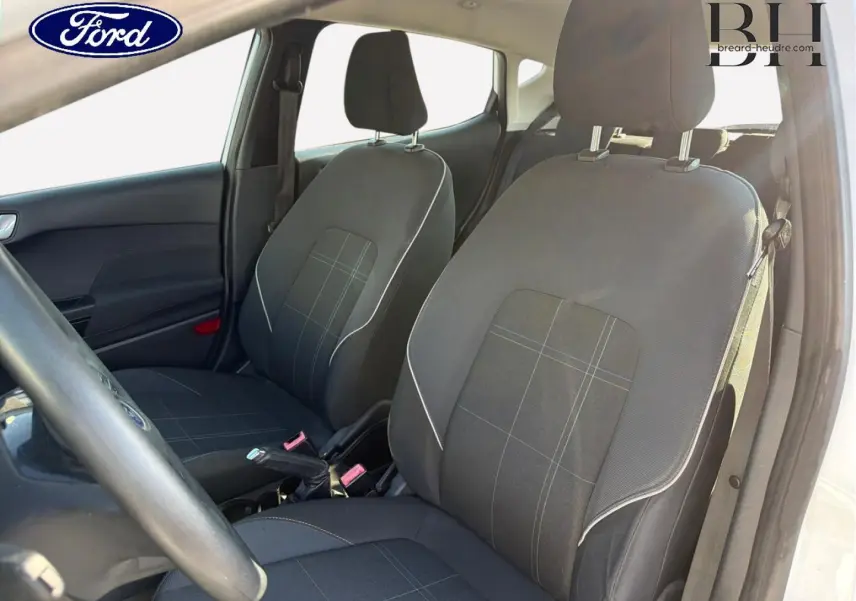 Vue intérieure côté conducteur de la Ford Fiesta 2018, montrant les sièges en tissu noir à motifs gris et la console centrale.