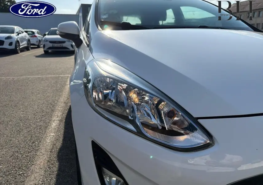 Gros plan sur l'avant droit blanc glacier d'une Ford Fiesta 2018, mettant en valeur le phare et le rétroviseur.