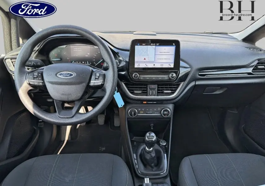 Vue intérieure frontale du tableau de bord et volant noir de la Ford Fiesta 2018 avec écran tactile et levier de vitesses manuel.