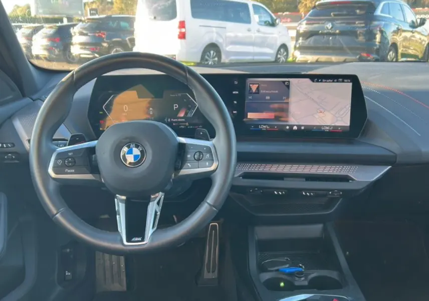 Vue intérieure centrée sur le volant BMW Série 1 2025 avec tableau de bord numérique et écran tactile.