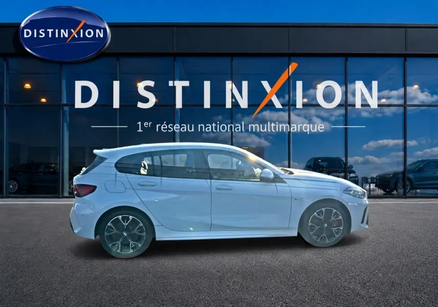 BMW Série 1 blanc alpin vue de profil côté gauche avec jantes 18 pouces bicolores devant une vitrine Distinxion.