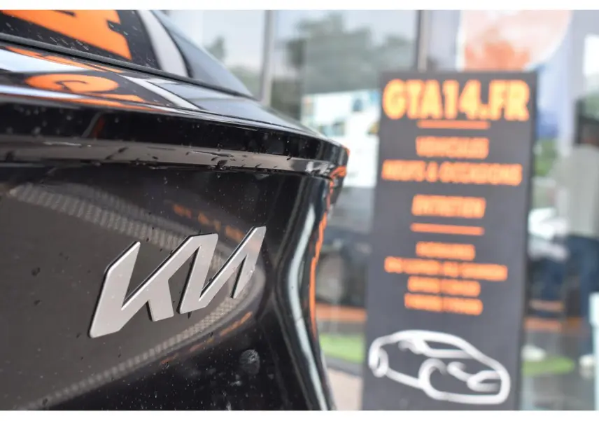 Gros plan sur le logo KIA à l'arrière d'un Kia Sportage noir, avec reflet et panneau flou en arrière-plan.