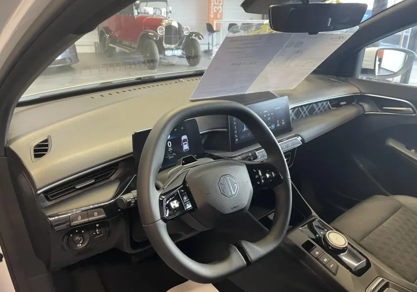 Vue intérieure côté conducteur du MG3 1.5 Hybrid+ blanc, volant multifonction et écran tactile central visibles.