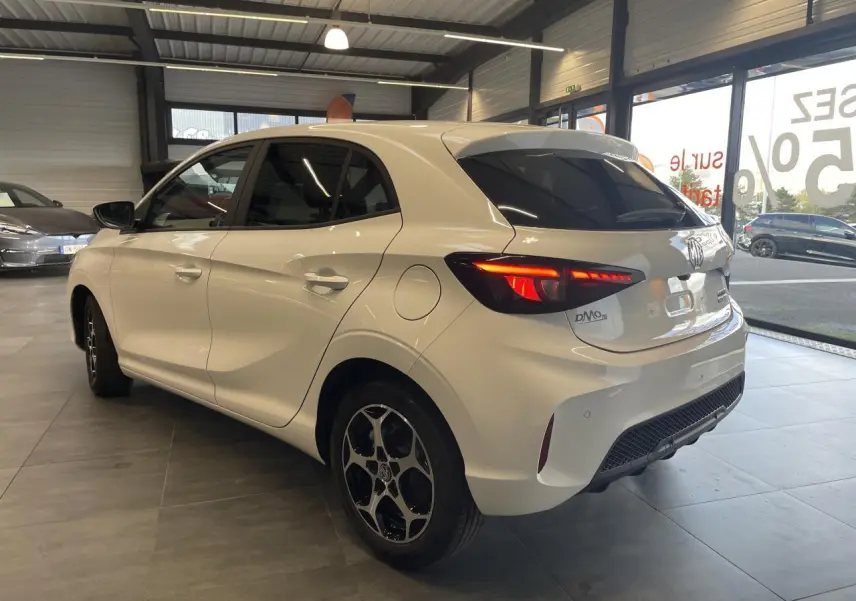 Vue 3/4 arrière côté droit d'une MG3 blanche avec feux arrière LED allumés en showroom.
