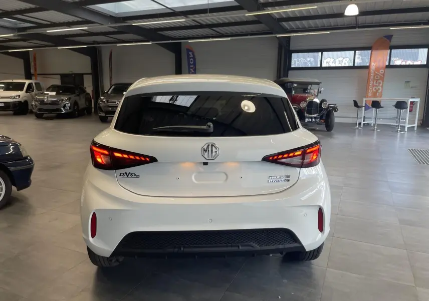 Vue arrière d'une MG3 1.5 Hybrid+ blanche avec feux LED allumés dans un showroom intérieur.