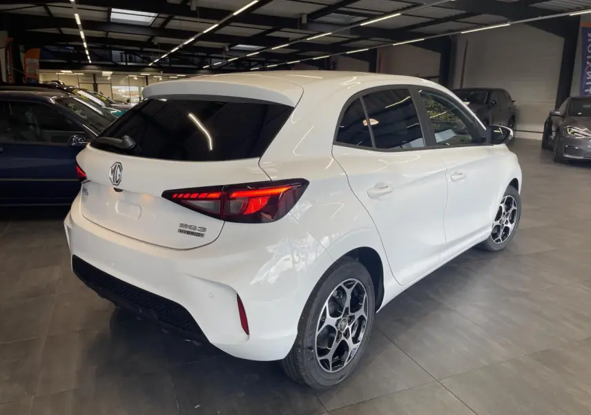 Vue 3/4 arrière droite d'une MG3 blanche avec feux LED allumés et jantes alliage noires en showroom.