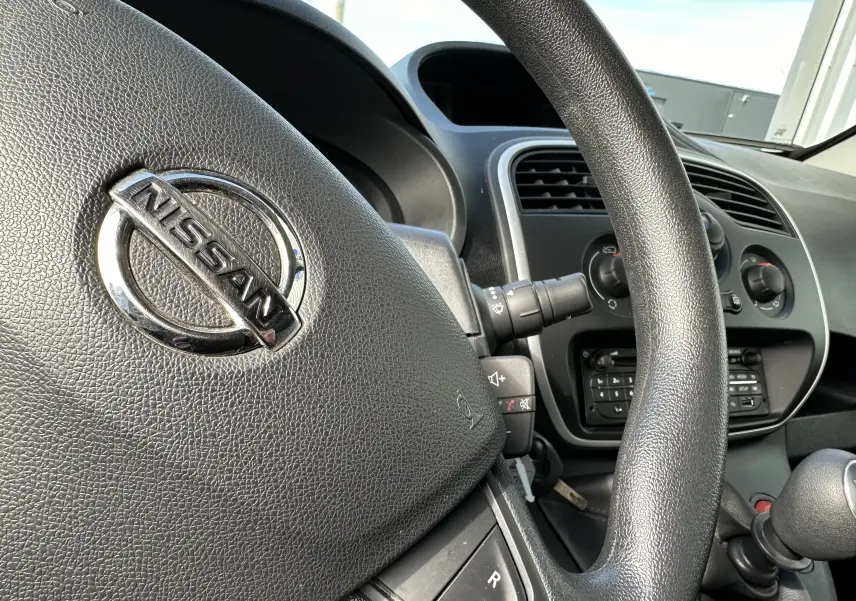 Gros plan sur le volant noir avec logo Nissan, tableau de bord et commandes centrales du Nissan NV250 blanc de 2020.