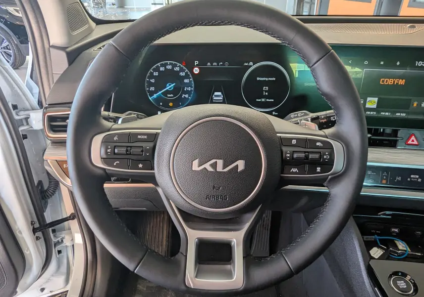 Vue rapprochée du volant cuir noir du Kia Sportage blanc MY25 avec tableau de bord digital et écran tactile.