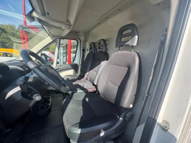Vue intérieure côté conducteur du Peugeot Boxer Fourgon blanc Banquise, montrant les sièges avant en tissu gris et le volant.