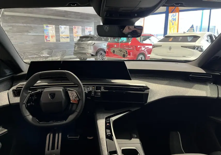Vue intérieure avant du Peugeot 3008 gris titanium 2025, avec tableau de bord moderne et volant compact noir.