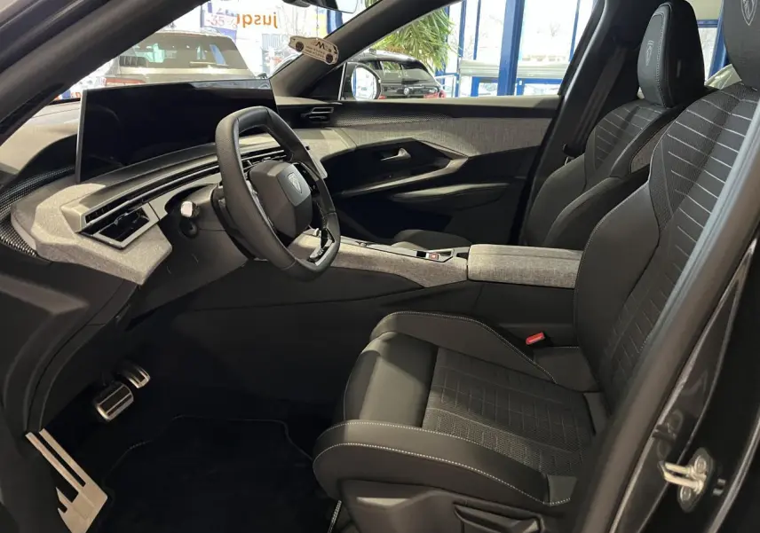 Vue intérieure côté conducteur du Peugeot 3008 gris titanium 2025, avec sièges tissu et volant compact noir laqué.