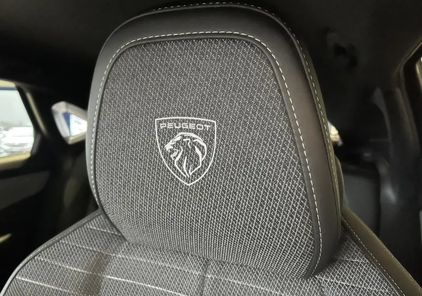 Gros plan sur l'appuie-tête avant avec logo Peugeot brodé sur tissu gris chiné, intérieur noir du 3008 GT 2025.