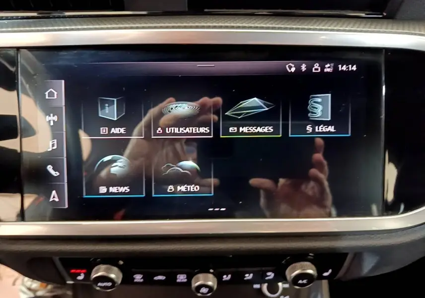 Écran tactile central de l'Audi Q3 gris foncé, affichant le menu principal avec options d'aide et messages.