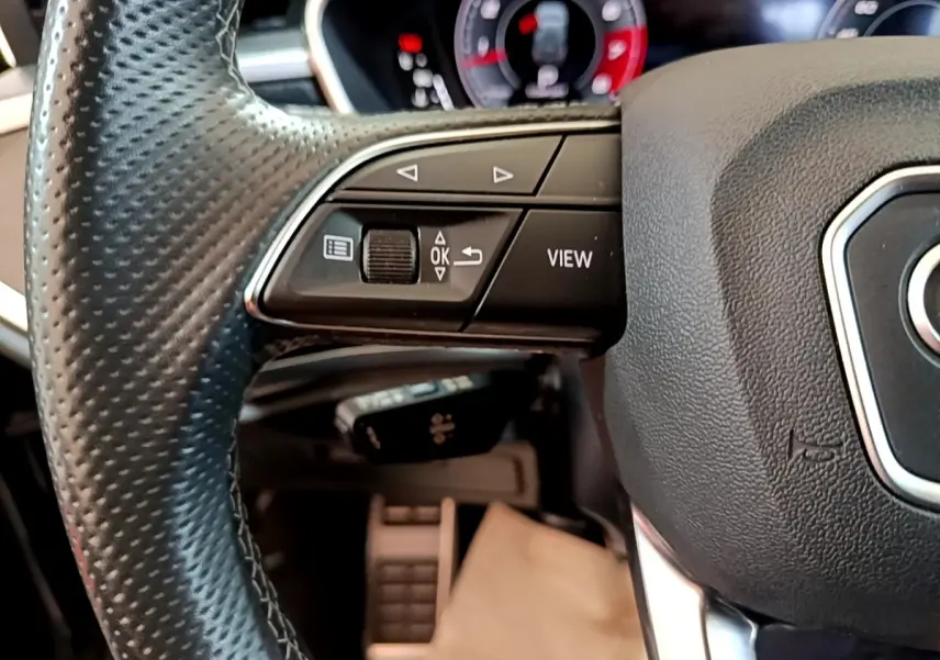 Gros plan sur le volant cuir noir de l'Audi Q3 35 TFSI, avec commandes multifonctions et tableau de bord numérique en arrière-plan.