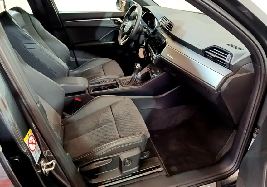 Vue intérieure côté conducteur de l’Audi Q3 gris foncé 35 TFSI S Line avec tableau de bord moderne et sièges en tissu.