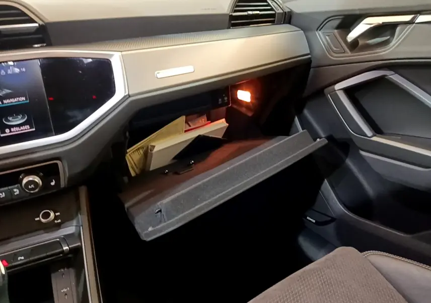 Intérieur de l’Audi Q3 35 TFSI S Line 2022, vue côté passager avec boîte à gants ouverte et tableau de bord gris foncé.