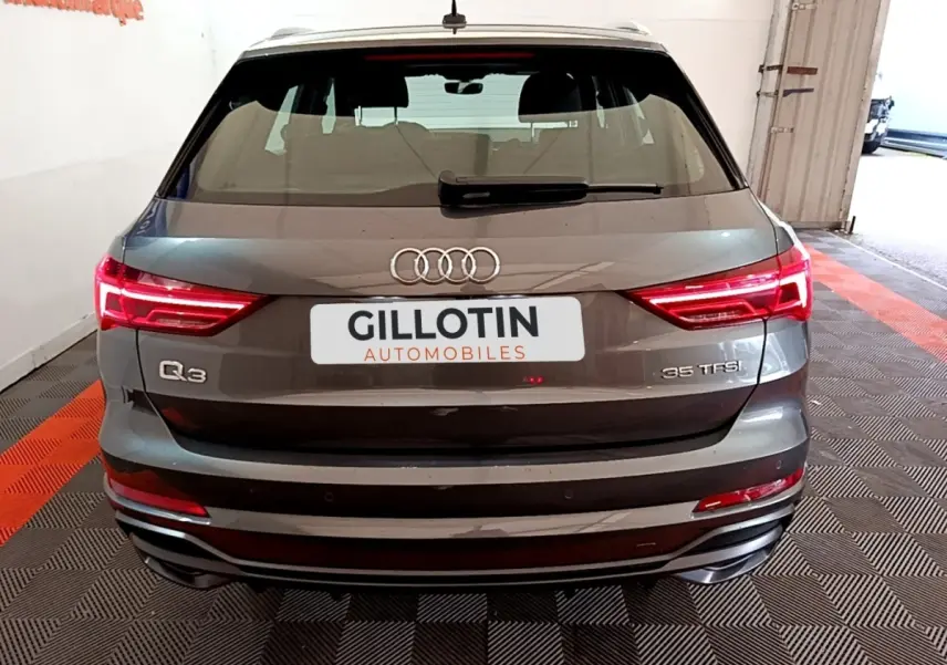 Vue arrière d'un Audi Q3 gris foncé 35 TFSI avec feux LED allumés dans un garage fermé.