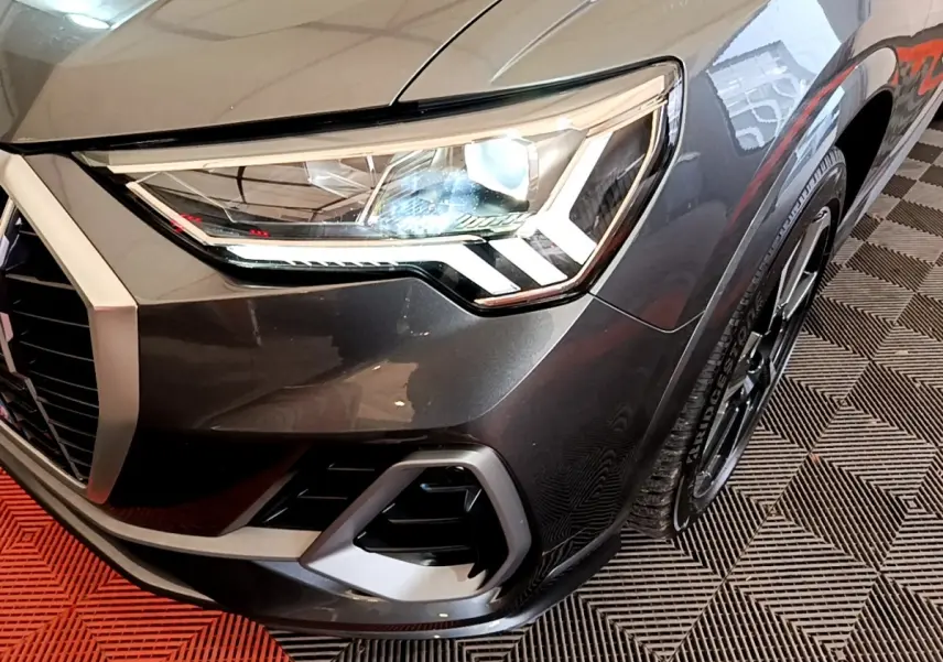 Gros plan sur l'avant droit gris foncé de l'Audi Q3 35 TFSI S LINE, mettant en valeur son phare LED et la calandre.