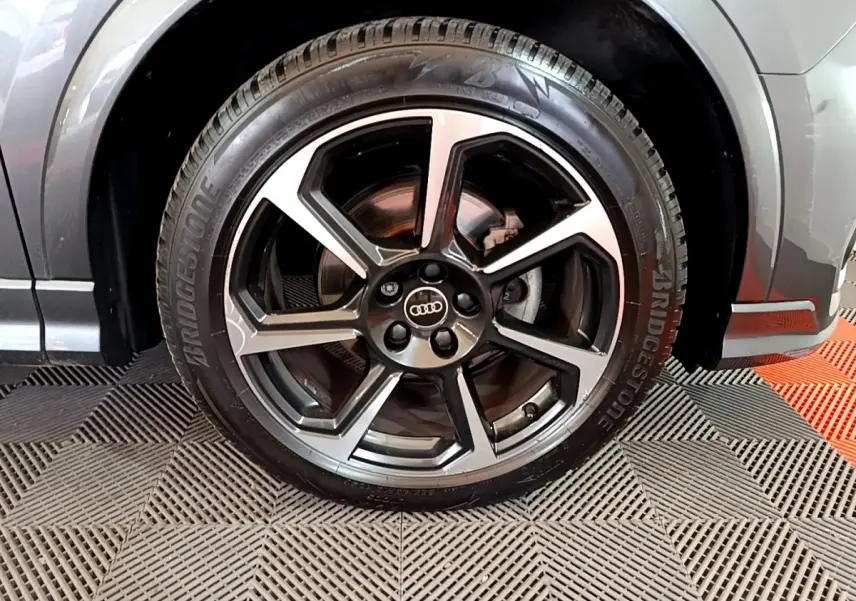 Gros plan sur la roue avant droite d’un Audi Q3 gris foncé, avec jante alliage à cinq branches doubles.