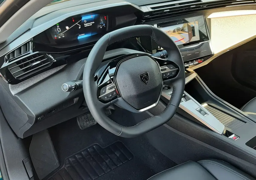 Vue intérieure côté conducteur de la Peugeot 308 2026, volant compact, tableau de bord numérique et écran central affichant la caméra 360°.