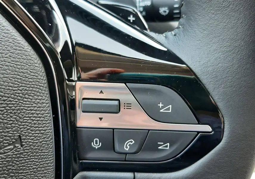 Gros plan sur les commandes multifonctions noires à gauche du volant en cuir d'une Peugeot 308 2026.