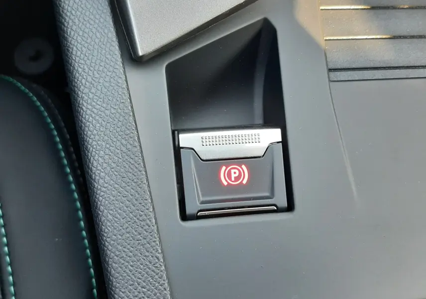 Gros plan sur le bouton de frein à main électronique rouge dans l'habitacle noir de la Peugeot 308 Bleu Obsession.