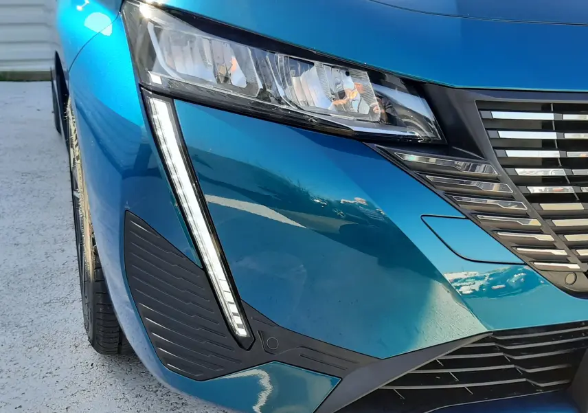 Gros plan sur l'avant droit bleu obsession du Peugeot 308 2026, mettant en valeur le phare et la calandre distinctive.