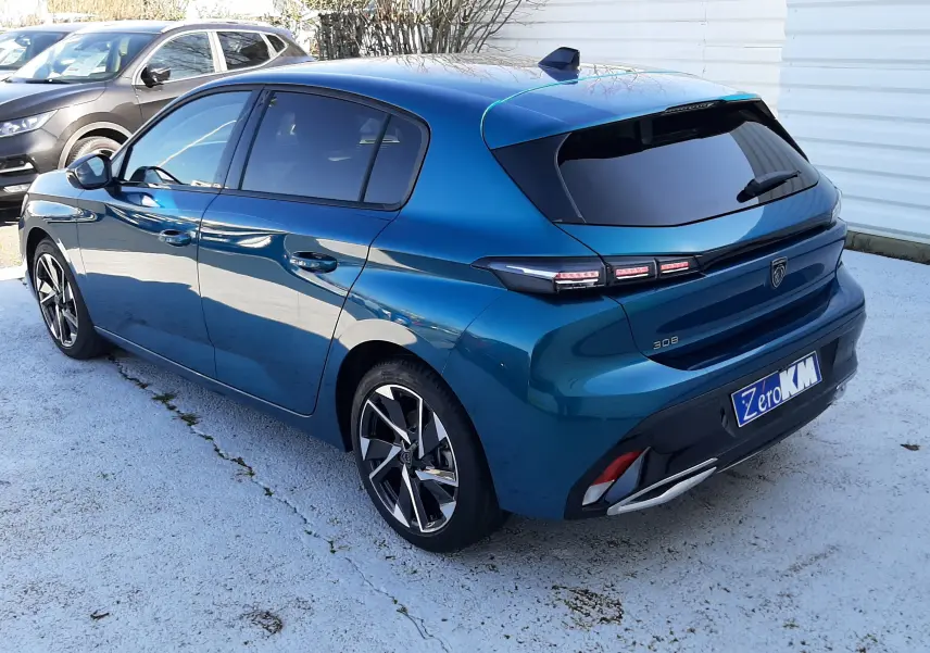 Vue 3/4 arrière droite d'une Peugeot 308 Bleu Obsession avec feux arrière distinctifs et jantes alliage bicolores.