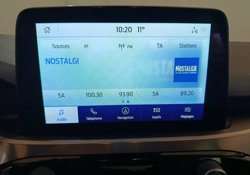 Écran tactile central affichant la radio Nostalgie dans l'habitacle du Ford Kuga gris foncé, vue de face.