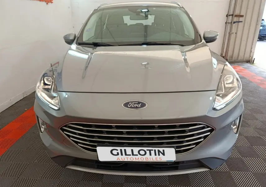 Vue avant d'un Ford Kuga gris foncé 2023 avec calandre chromée et phares LED allumés en intérieur showroom.