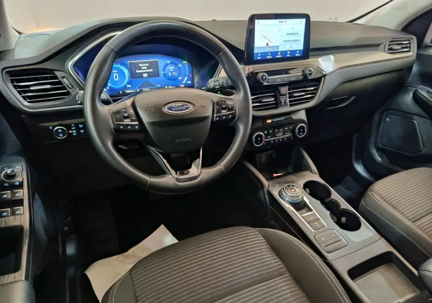 Vue intérieure avant du Ford Kuga 2023 gris foncé, volant cuir multifonctions et écran tactile central visible.
