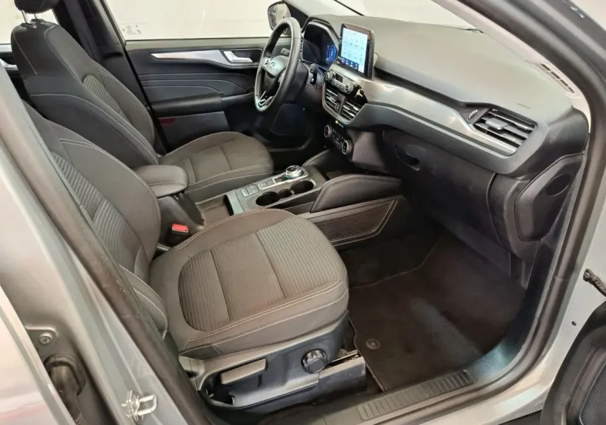 Vue intérieure côté conducteur du Ford Kuga 2023, sièges tissu gris foncé et écran tactile central visible.