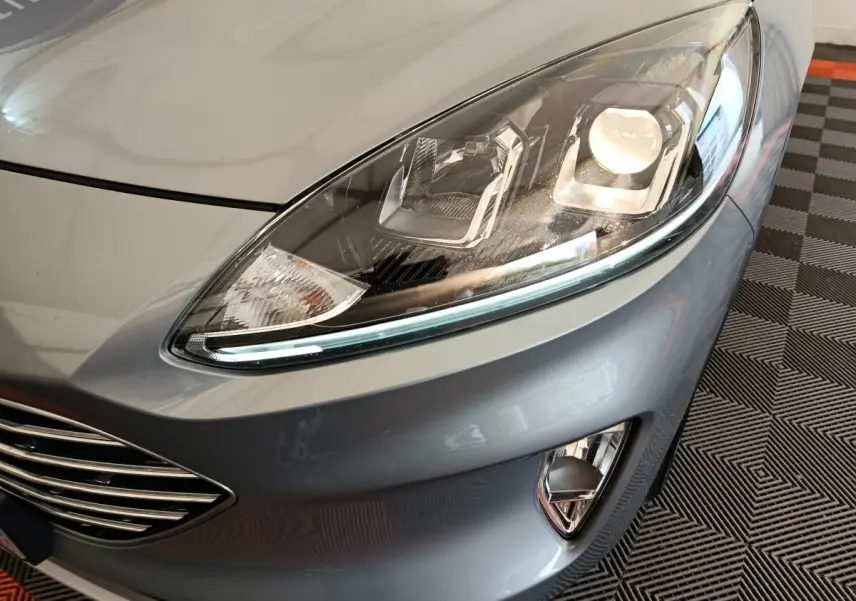Gros plan sur le phare avant droit et la calandre d’un Ford Kuga gris foncé 2023, avec antibrouillards intégrés.