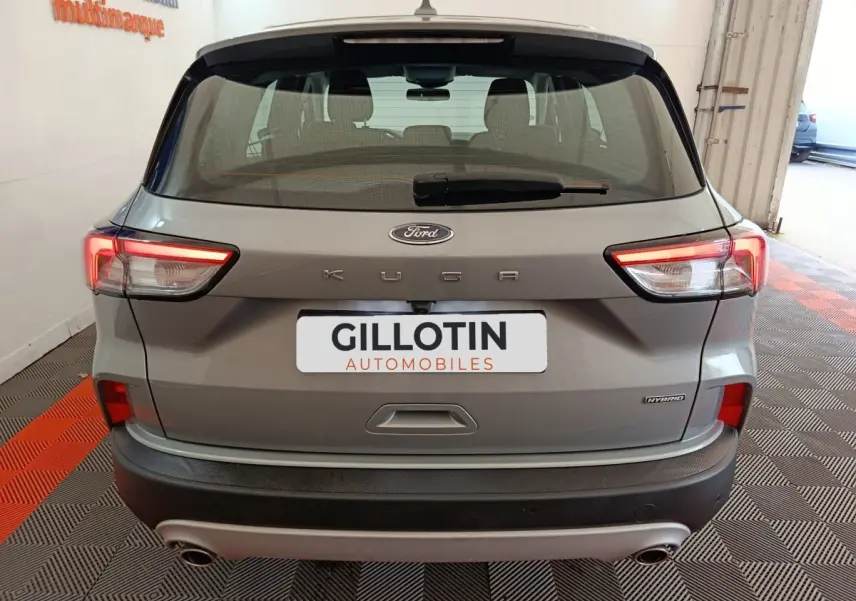 Vue arrière d’un Ford Kuga gris foncé hybride 2023 avec feux LED allumés et double sortie d’échappement visible.