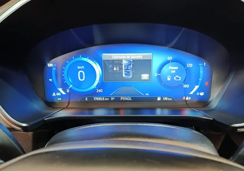 Vue rapprochée du combiné d'instruments numérique bleu du Ford Kuga 2023, affichant la vitesse et alertes de sécurité.