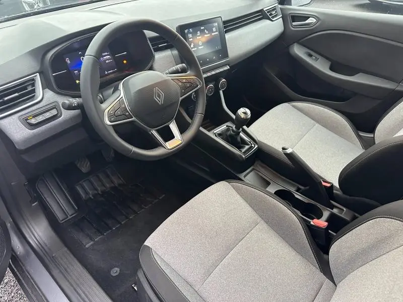 Vue intérieure avant droite de la Renault Clio 2025 essence, montrant volant, tableau de bord numérique et sièges gris clair.