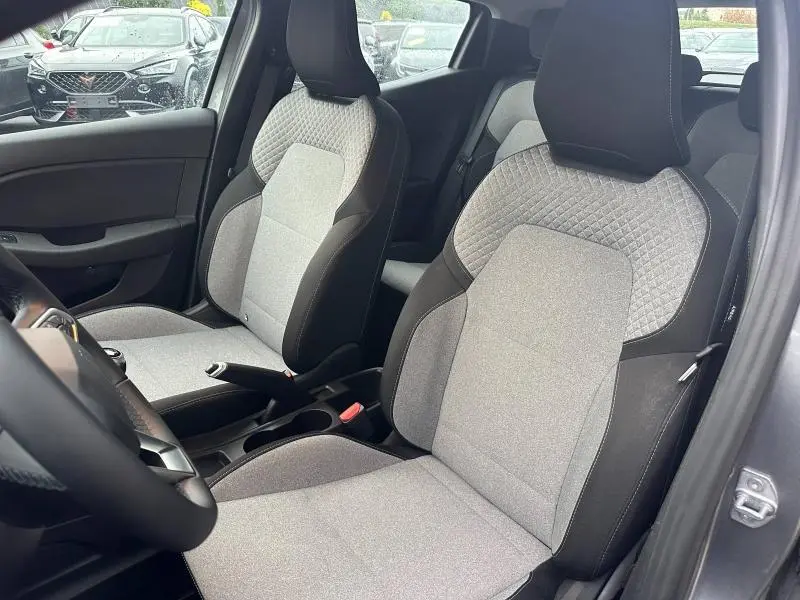 Vue intérieure côté conducteur de la Renault Clio 2025, sièges tissu gris clair avec surpiqûres losangées et détails noirs.
