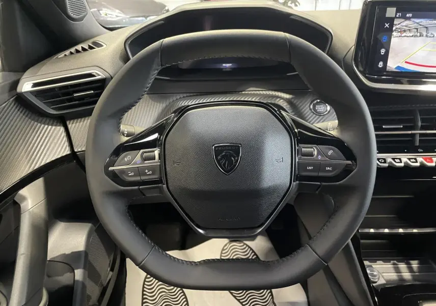 Vue intérieure centrée sur le volant compact noir du Peugeot 2008 1.2i Hybrid 2026 avec tableau de bord carbone.