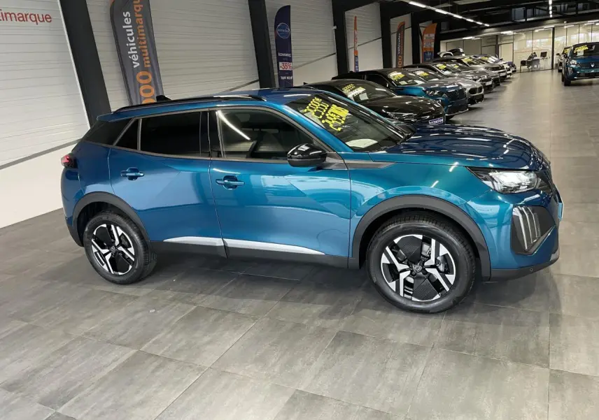 Peugeot 2008 hybride bleu en vue profil droit dans un showroom, avec jantes alliage bi-ton et barres de toit noires.
