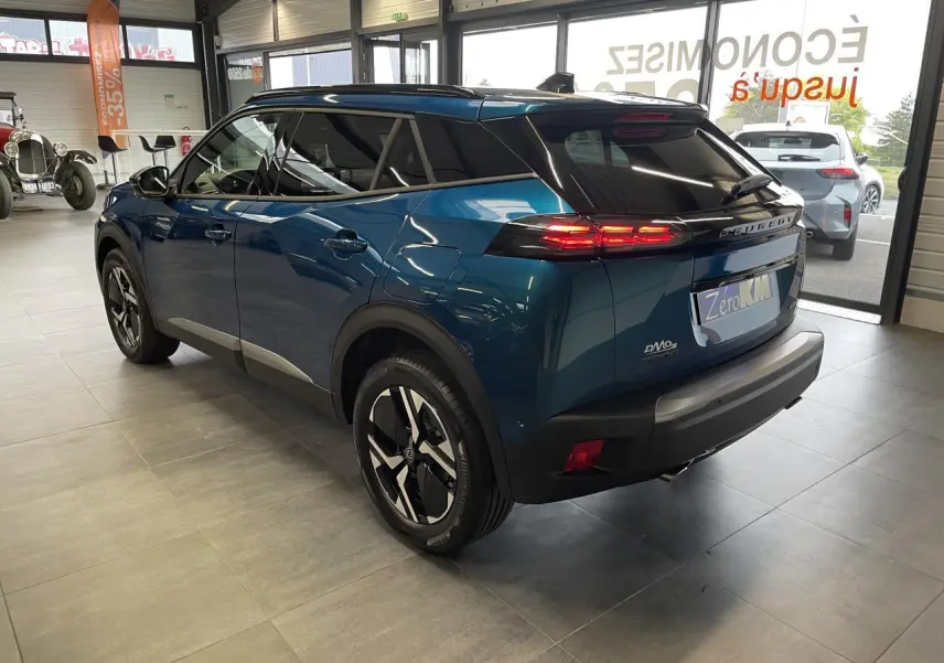 Vue 3/4 arrière droite d'un Peugeot 2008 bleu métallisé avec toit noir et jantes alliage bi-ton en showroom.