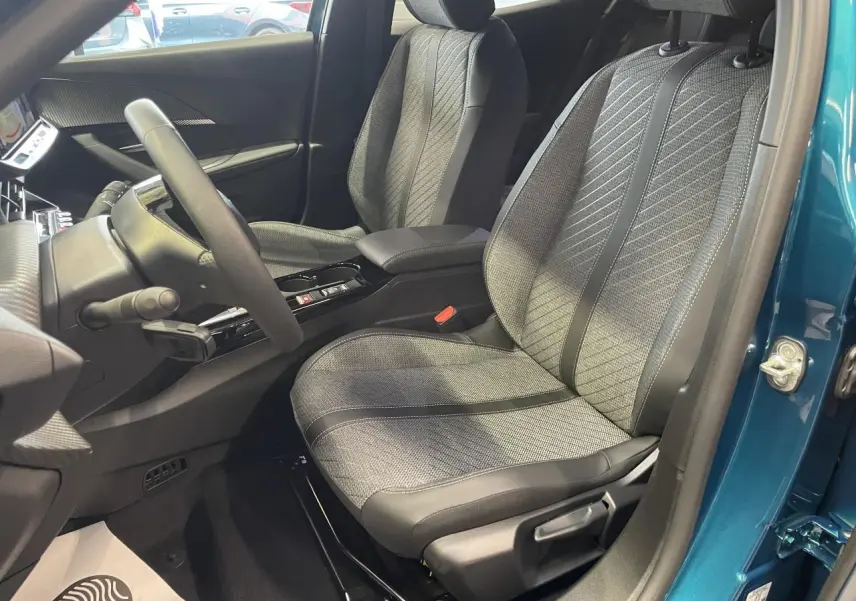 Vue intérieure côté conducteur du Peugeot 2008 bleu, mettant en valeur le siège tissu gris et la console centrale noire brillante.