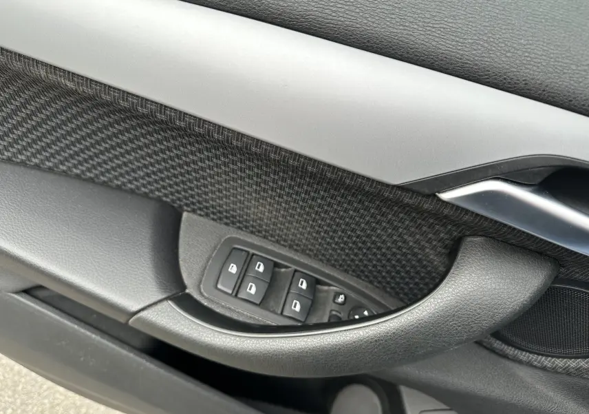 Gros plan sur la commande des vitres et la poignée intérieure côté gauche d'une BMW X2 gris 2018.