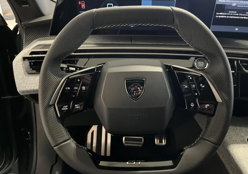 Vue rapprochée du volant compact noir perforé avec logo Peugeot et badge GT du Peugeot 3008 gris titanium 2025.