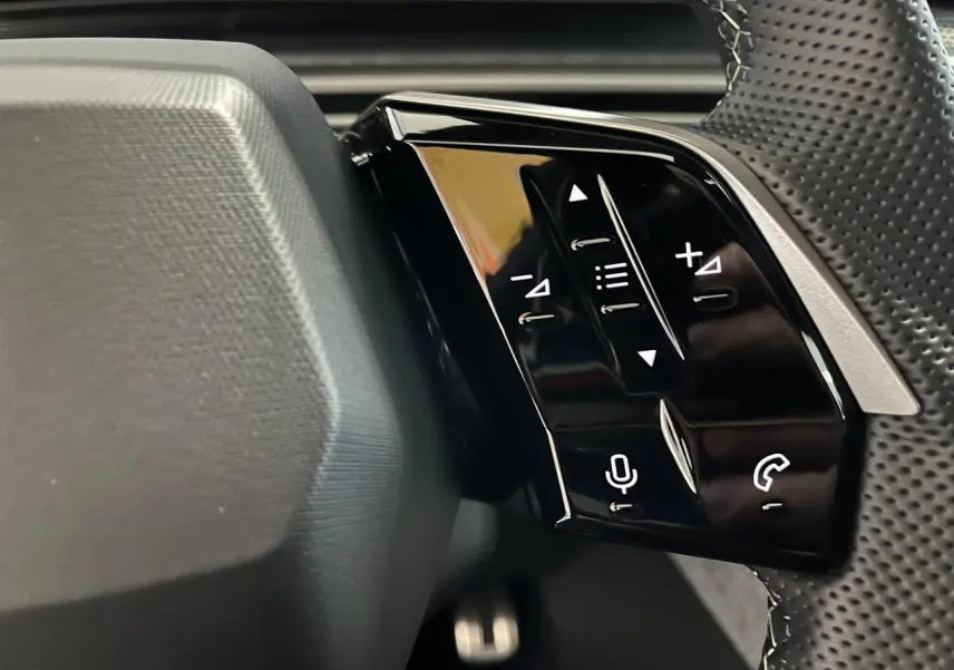 Gros plan sur les commandes noires brillantes du volant perforé du Peugeot 3008 gris titanium 2025 GT.