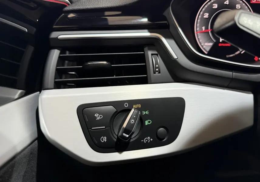Détail du tableau de bord côté gauche d'une Audi A4 gris foncé 2022 avec commande d'éclairage en mode auto.
