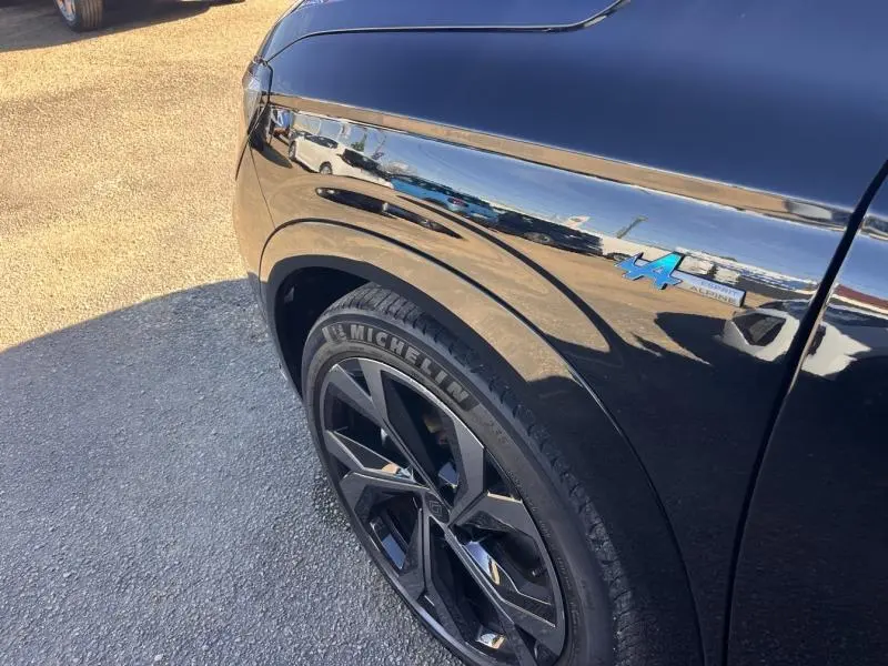 Gros plan sur l’aile avant gauche noire étoilée du Renault Austral avec badge Alpine bleu et jante alu noire.