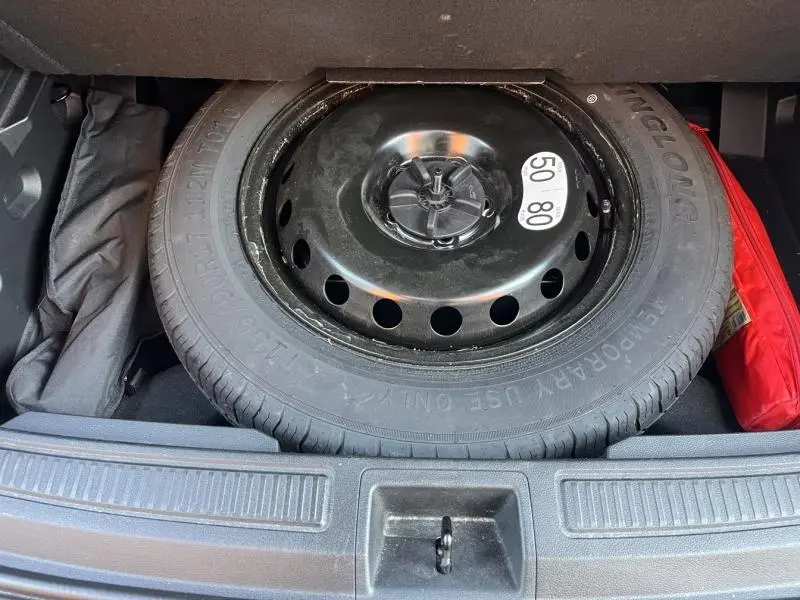 Vue plongeante sur la roue de secours noire dans le coffre du Renault Austral noir étoilé 2023, entourée d'accessoires.