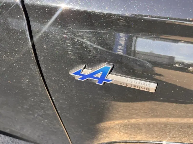 Gros plan sur l'emblème Esprit Alpine bleu sur la carrosserie noir étoilé d'un Renault Austral 2023.
